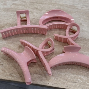 Detail showing five light pink geometric hair claw clips with shiny finish on stone background