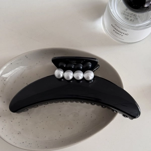 Detalle de una pinza para el pelo negra en forma de luna con perlas blancas y negras