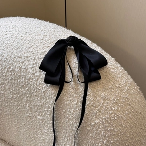 Elegant black satin rose bow hair clip with long ribbons on soft cream texture background