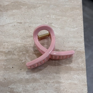 Detailed top view of a pink glossy claw clip with elegant ribbon twist and golden spring