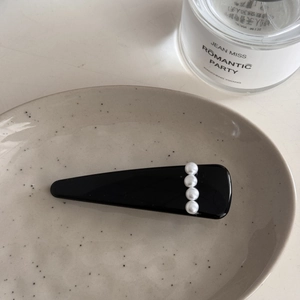 Vista detallada de pinza para el pelo negra con cuatro perlas sobre plato cerámico