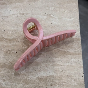 Detailed top view of a glossy light pink hair claw clip with golden metal spring on marble