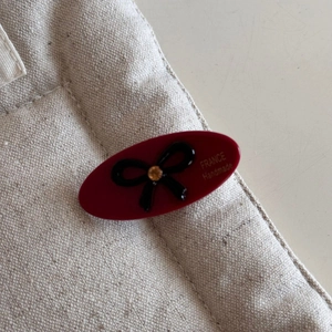 Detail of a handmade burgundy oval hair clip with black bow and sparkling yellow crystal