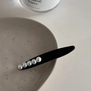 Elegante pinza para el pelo negra con cinco perlas blancas sobre fondo de cerámica