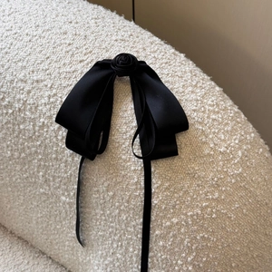 Detail of a black satin bow hair clip featuring a delicate 3D rose on soft fleece fabric