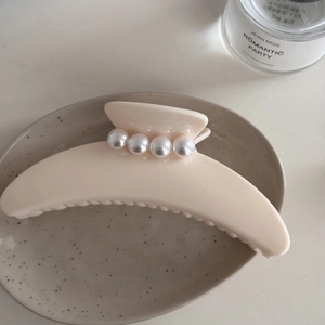 Primer plano de una pinza para el cabello beige crema con perlas en un plato cerámico