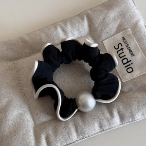 Close-up of black fabric scrunchie with white trim and a large pearl on linen bag