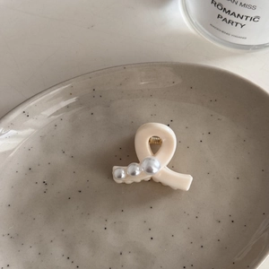 Detalle de una pinza para el cabello color crema con perlas en una bandeja de cerámica