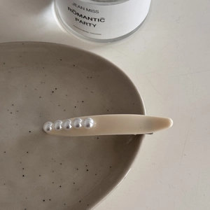 Detalle de una elegante pinza para el pelo con perlas beige sobre un plato decorativo