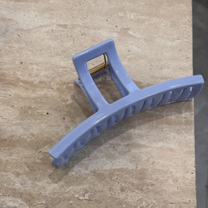 Detail of light blue hair claw clip with golden metal spring on marble surface