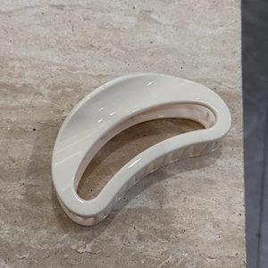 Gros plan d'une pince à cheveux minimaliste blanc crème sur surface en pierre