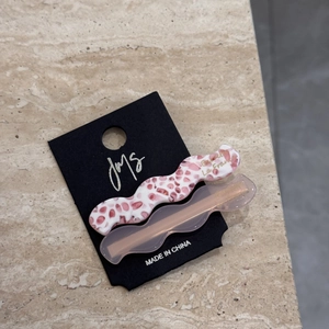 Detail of two wavy acetate hair clips in pink floral and translucent finish on card