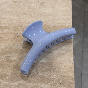 Close-up of large lavender shark hair claw clip on a textured beige stone background