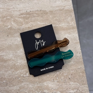 Detailed macro view of two wavy acetate hair clips in brown and green on a black display card