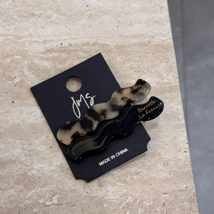 Detailed view of wave-shaped acetate hair clips in tortoise shell and black on display card