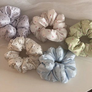 Close-up of five colorful polka dot satin scrunchies in pastel purple, green, and blue