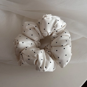 Detail of soft cream satin scrunchie with black polka dots and pleated fabric texture