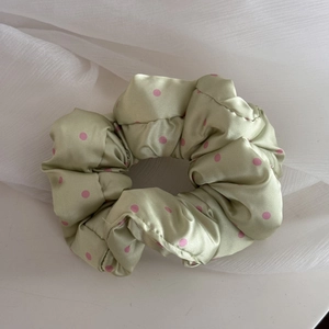 Macro detail of a soft padded satin scrunchie with pink polka dots on light green fabric
