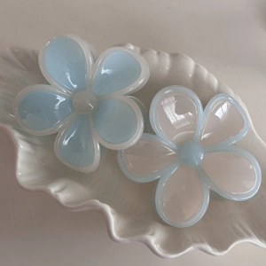 Nahaufnahme von zwei Blumen-Haarklammern in Blau und Weiß auf einer Schalenablage