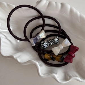 Five styles of small acetate bow elastic hair ties on a shell tray for daily use