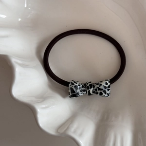 Detail view of a black elastic hair tie with a spotted acetate bow on a ceramic dish