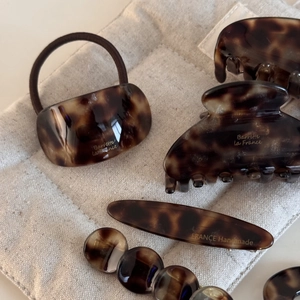 Macro detail of tortoiseshell acetate hair clips and accessories on a beige textured base