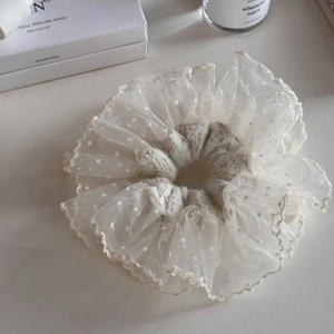 Detail of elegant white lace scrunchie with polka dots and ruffled embroidered edges