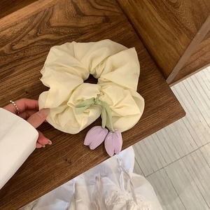 Detail of cream scrunchie with purple tulip flower charms on a rustic wooden shelf