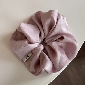Makrodetail eines rosa Satin-Haargummis mit silbernen Pailletten und kleinem Etikett
