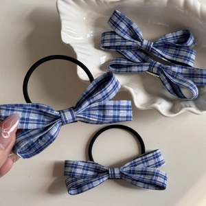 Detailed close-up of blue and white gingham bow hair clip and elastic hair tie in hand