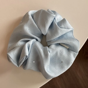 Detailansicht eines hellblauen Stoff-Scrunchies mit Pailletten und weißem Innenetikett