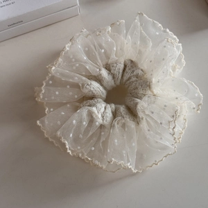 Close-up of cream lace scrunchie with white polka dots and delicate scalloped embroidery