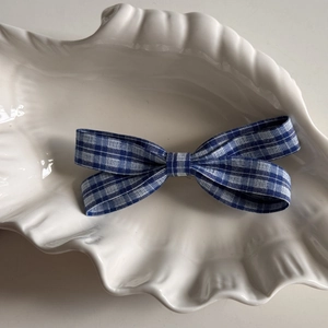 Close-up of blue and white plaid fabric bow hair clip on a decorative white shell tray