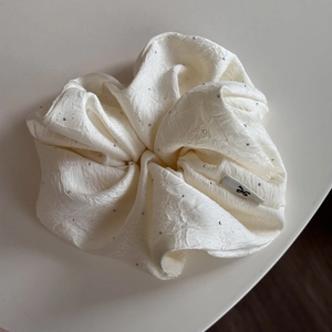 Detailaufnahme von weißem Krepp-Haargummi mit silbernen Strasssteinen und Etikett