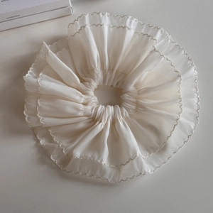 Macro detail of oversized ivory lace scrunchie with layered ruffles and wave stitching