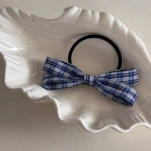 Detailed view of blue plaid bow hair tie resting on a white shell-shaped ceramic plate