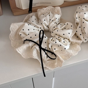 Detail of cream oversized scrunchie with heart print, lace trim and black velvet bow