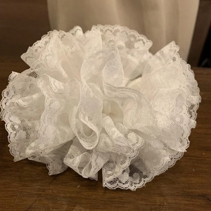 Dettaglio di uno scrunchie in pizzo bianco con balze su uno sfondo di legno scuro