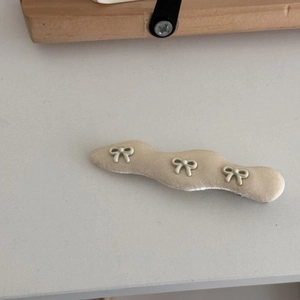 Detailaufnahme der gewellten beige Stoff-Haarklammer mit drei kleinen Schleifen-Dekoren