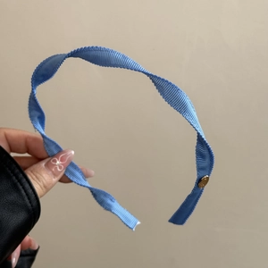 Detail of sky blue ribbed fabric headband with golden logo piece and wavy edge texture