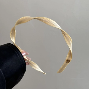 Close-up of spiral beige fabric headband with pleated texture and gold logo detail