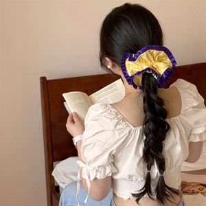 Détail d'un chouchou à carreaux jaunes avec dentelle violette sur une longue tresse femme