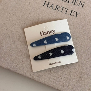 Detailed close-up of denim fabric hair clips with white heart patterns on beige linen