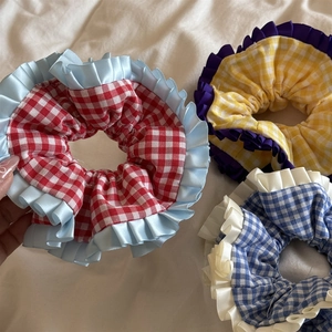 Détail de trois chouchous à carreaux avec bordures en dentelle satinée sur tissu plissé blanc