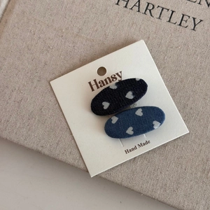 Close-up of two denim hair clips with heart patterns on a stylish paper card holder