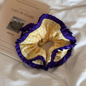 Détail d'un chouchou à carreaux jaunes avec dentelle violette sur un tissu blanc texturé