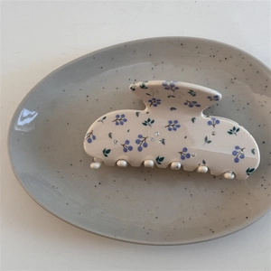 Détail d'une pince à cheveux crème avec motifs floraux violets et strass sur une assiette