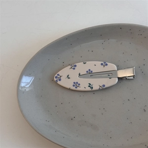 Détail d'une pince à cheveux crème à motifs de baies bleues sur plateau céramique
