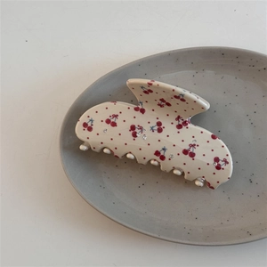 Détail d'une pince à cheveux crème avec imprimé cerise et nœud sur plat céramique