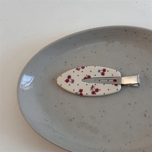 Détail d'une pince à cheveux blanche à motif cerises rouges avec attache métallique